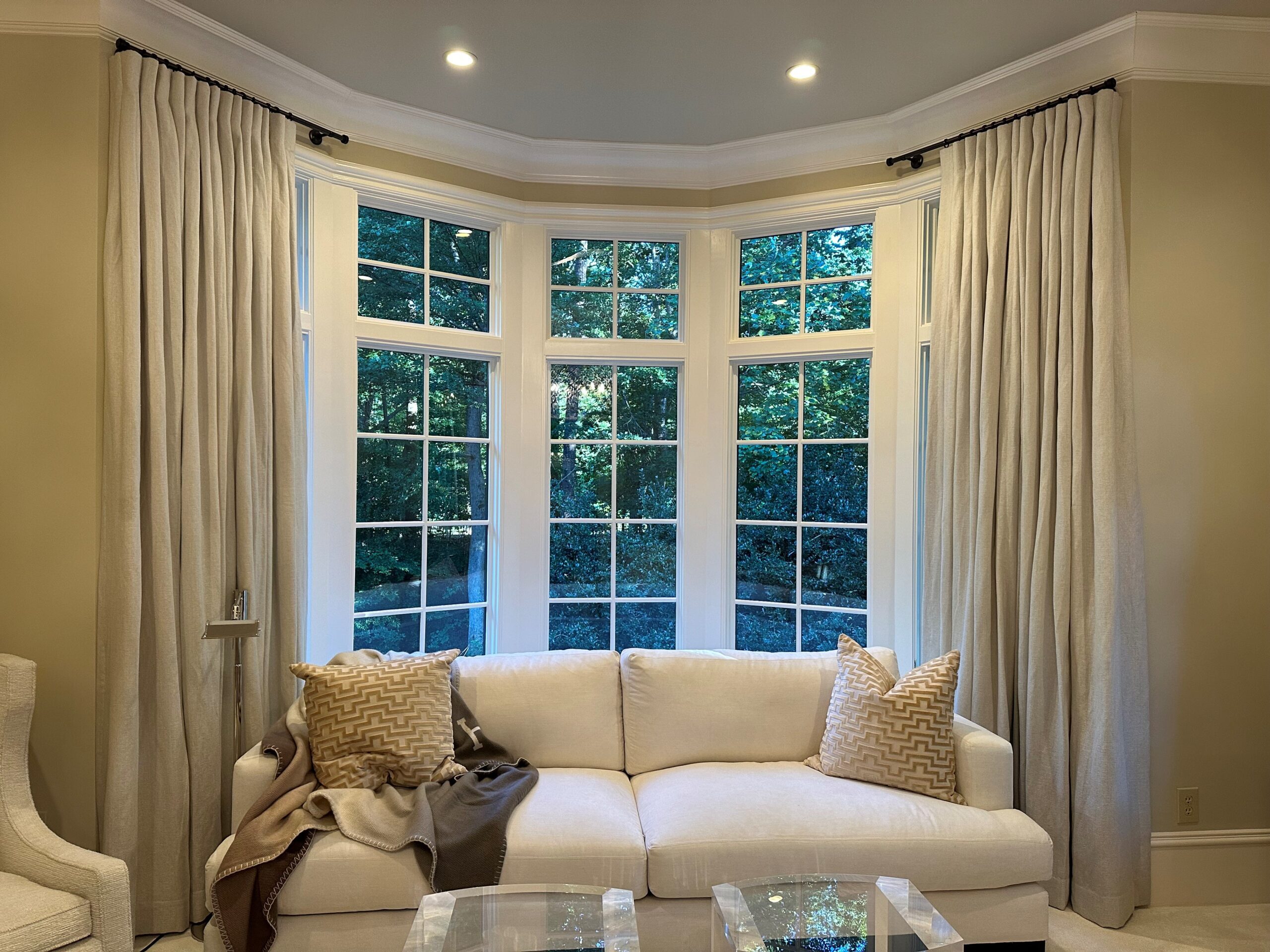 Elegant living room with large bay windows, beige drapes, and a white sofa.