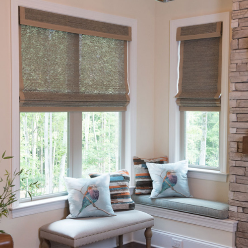 A small seating area with multi-colored pillows and windows that are partially covered by shades.